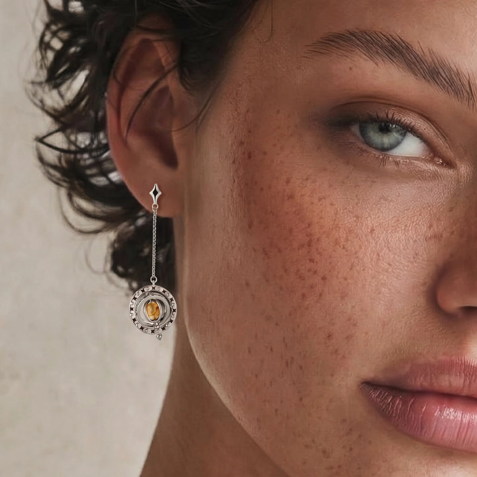 Asymmetrical earrings featuring a star-shaped post, honey-gold cabochon, and a silver-toned ring with black enamel stars.