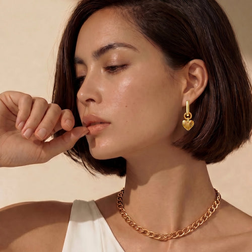 Gold-toned huggie earrings with a textured heart pendant, elegantly worn by a model.