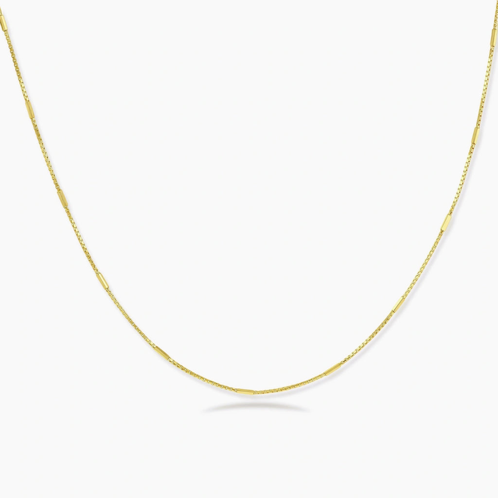 Delicate gold-plated sterling silver chain necklace with geometric segments displayed against cream background