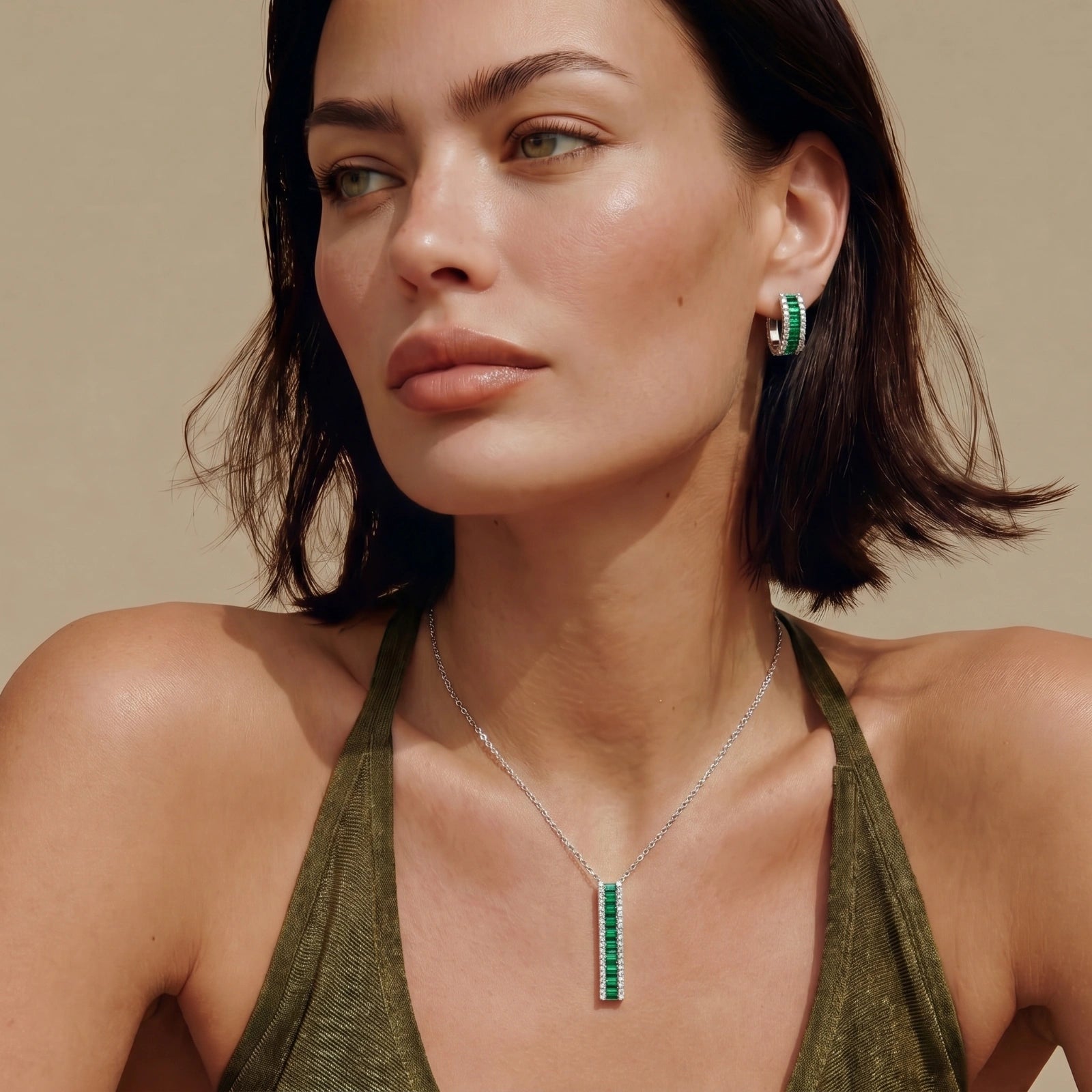 Model showcasing the Emerald Avenue Set, featuring a necklace with a vertical green element and matching huggie earrings.