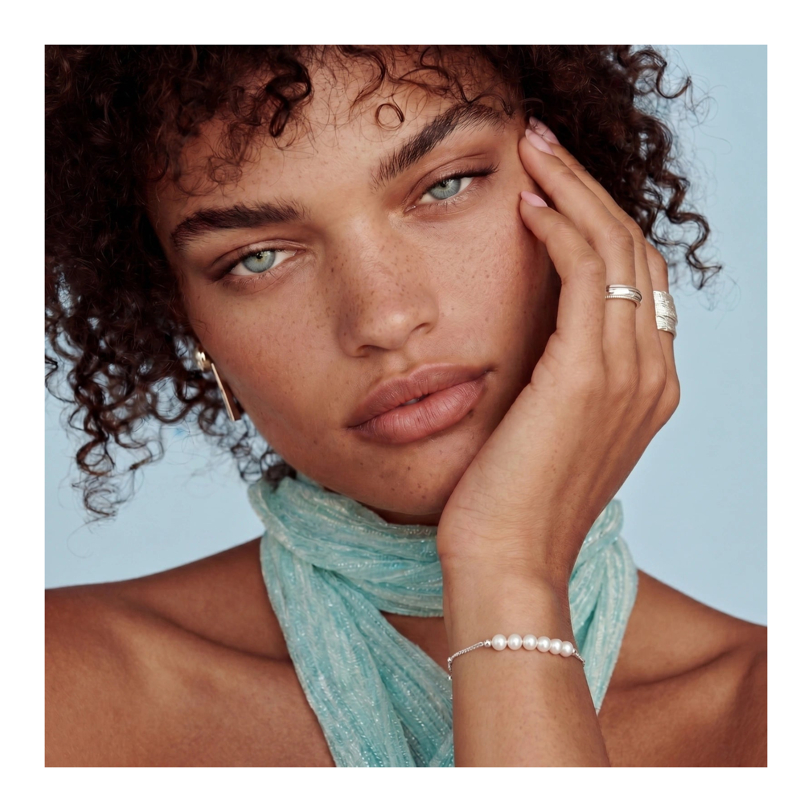 Delicate bracelet featuring six baroque pearls elegantly arranged, worn by a model with a light blue scarf against a soft blue background.