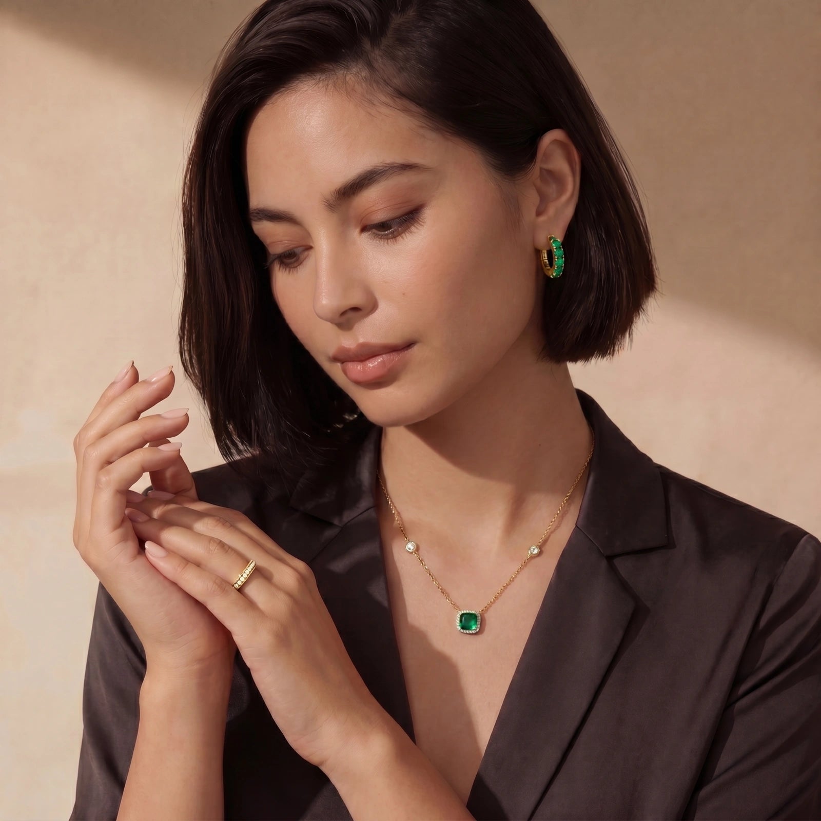 Elegant woman adorned with a gold chain necklace featuring a green cushion-cut pendant and a radiant halo, styled with a dark blazer.