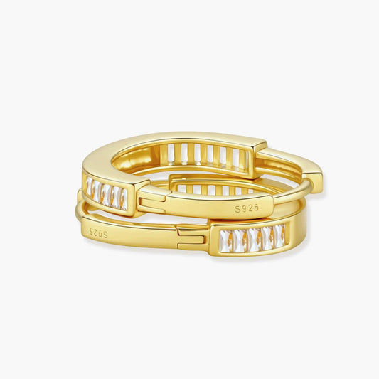 Close-up of gold-plated sterling silver huggie hoop earrings featuring rectangular cubic zirconia stones on neutral background.