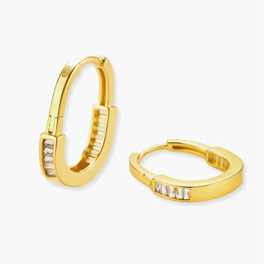 Huggie hoop earrings in gold finish adorned with a row of baguette-cut stones, featuring a secure hinged closure.