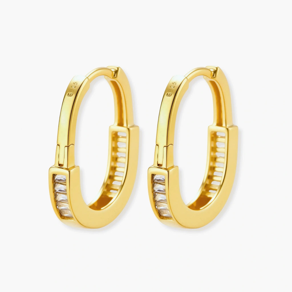 Close-up of gold-plated sterling silver huggie hoop earrings featuring rectangular cubic zirconia stones on neutral background.