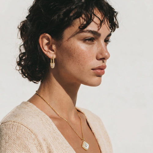 Polished gold huggie hoop earrings elegantly worn, showcasing their radiant zirconia detail against a softly blurred background.