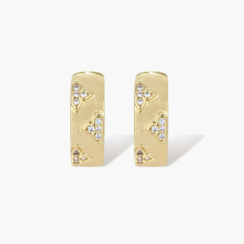 Gold-plated hoop earrings with textured surface and raised floral motifs set with clear zirconia stones on cream background.