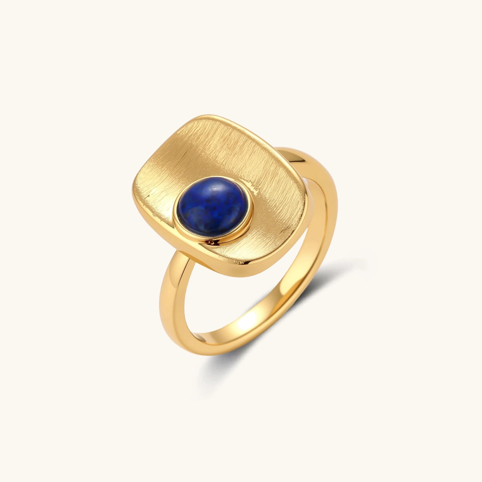 Brushed gold-plated ring featuring a central lapis lazuli cabochon set in a textured cushion design.