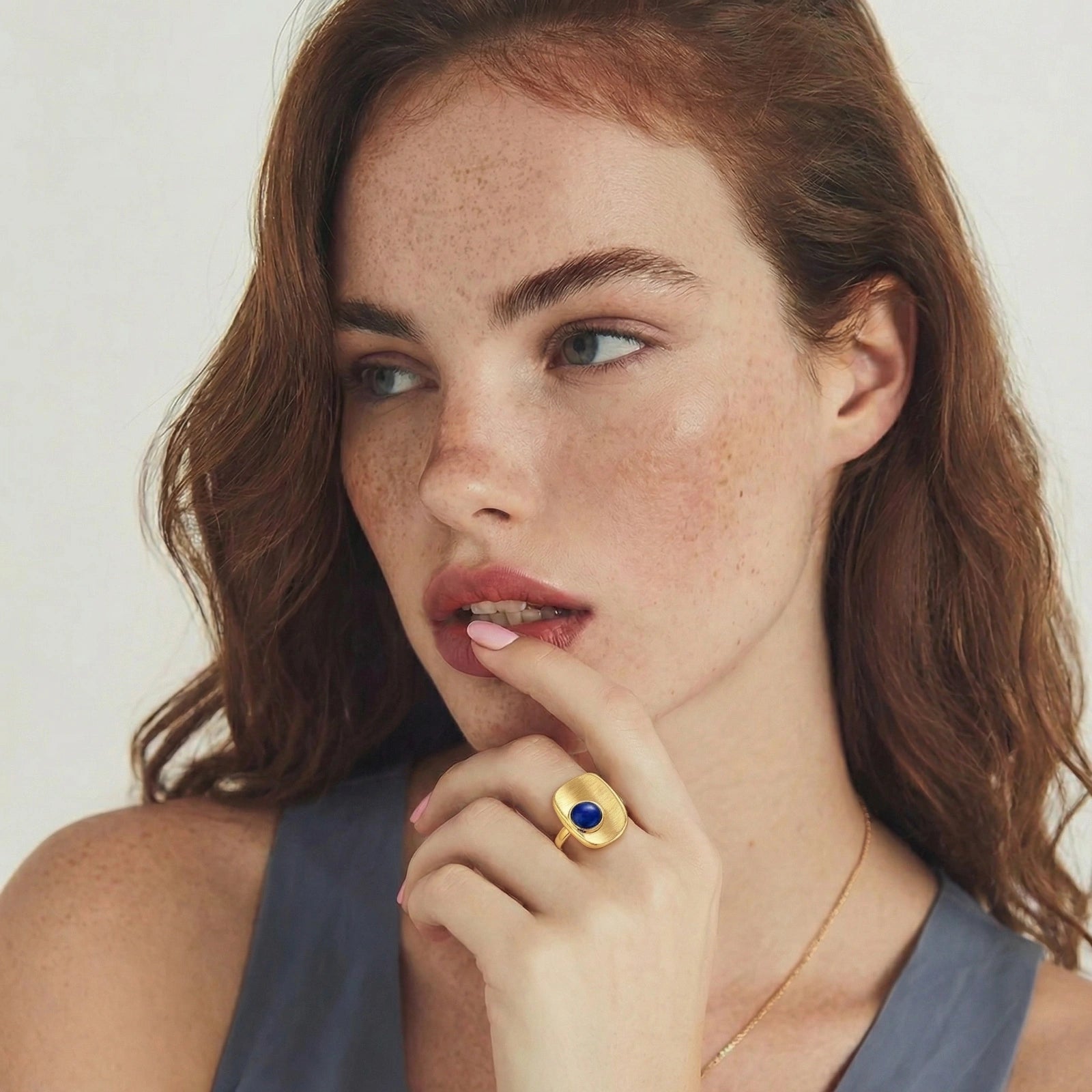 Brushed gold-plated ring featuring a textured surface and a central lapis lazuli cabochon, elegantly worn on a finger.