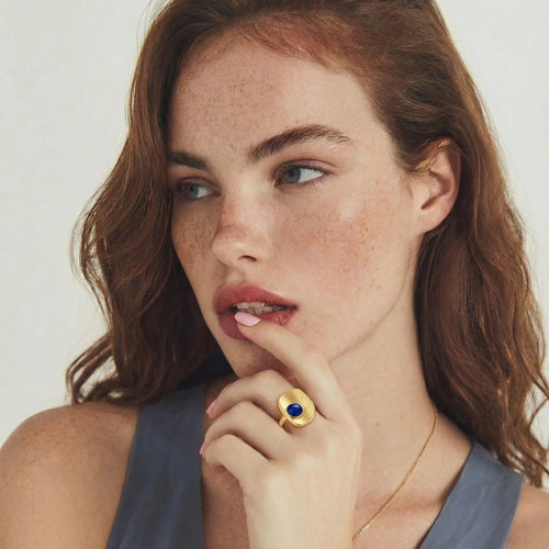 Brushed gold-plated ring featuring a textured surface and a central lapis lazuli cabochon, elegantly worn on a finger.