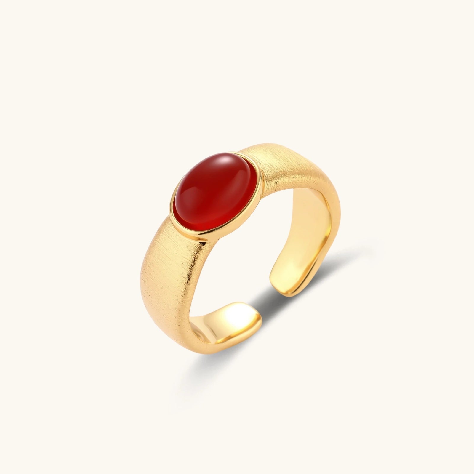 Brushed gold ring featuring a polished oval red cabochon, designed with an adjustable band for a perfect fit.