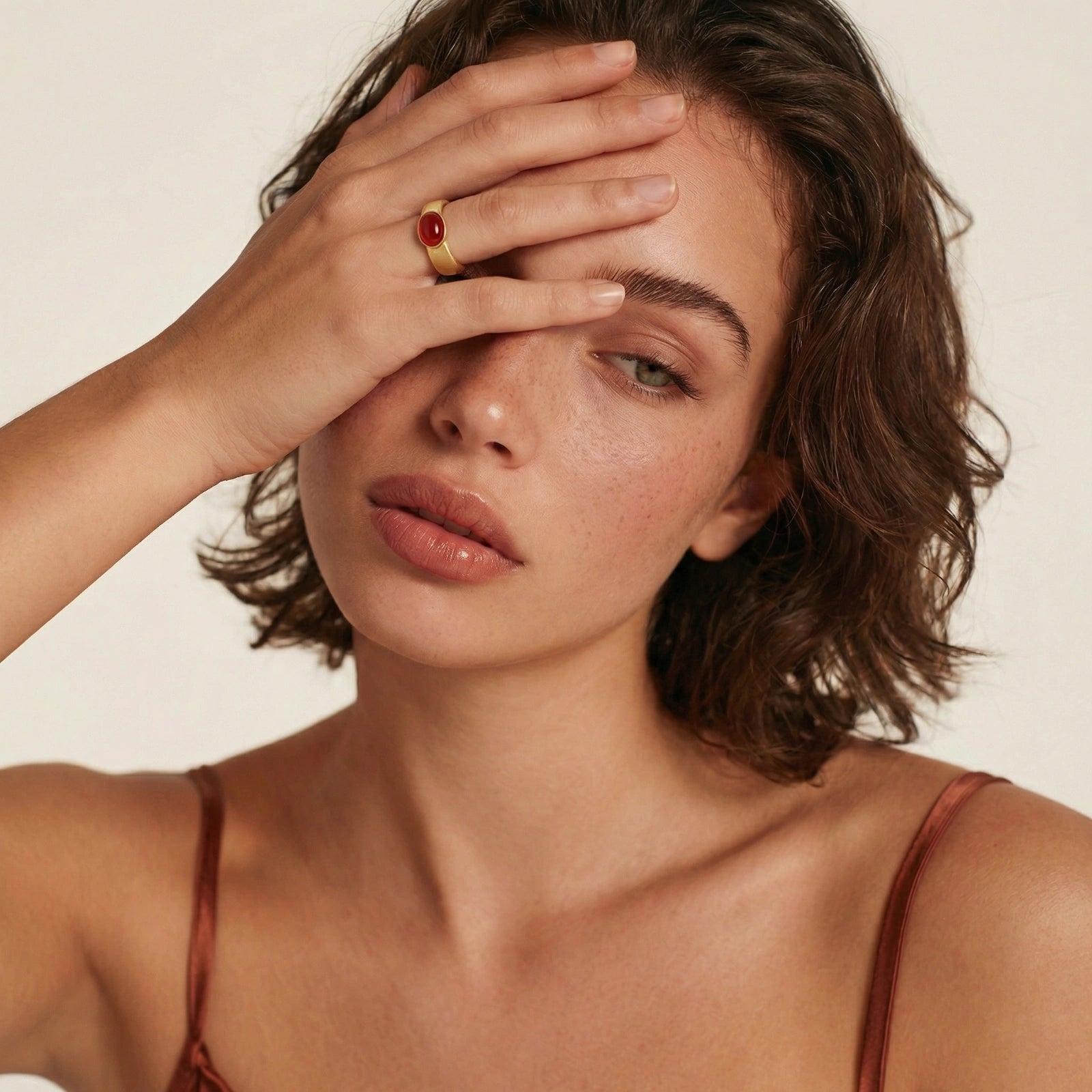 Brushed gold adjustable ring adorned with a polished oval red cabochon, elegantly worn on a model's hand.