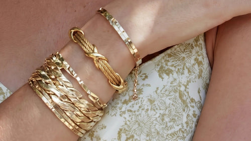 Twisted cable bracelet in gold featuring polished X-shaped knots, elegantly worn alongside other bracelets.