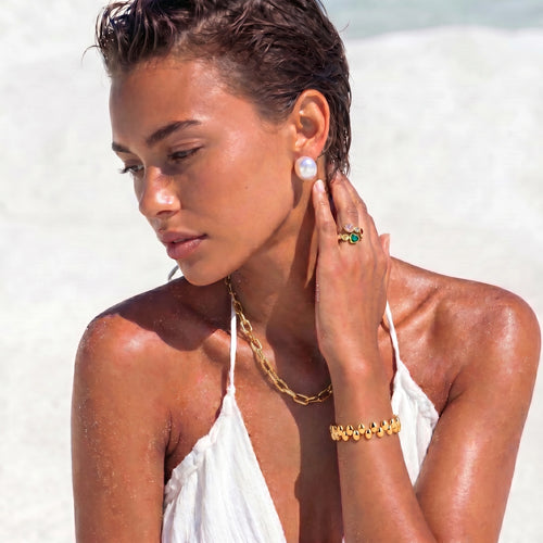 Model showcasing the Pebble Orbit Bracelet with a sculptural double-row design and glossy gold beads against a bright backdrop.