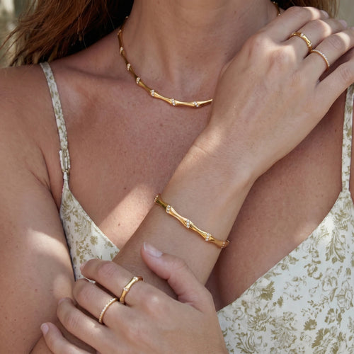 Wavy gold bangle adorned with sparkling clusters, elegantly styled on a wrist with a floral outfit.