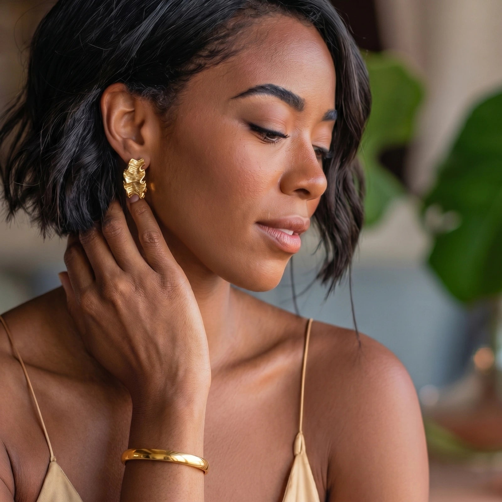 Slim, smooth bangle worn on a wrist, reflecting light elegantly, set against a natural backdrop of green plants.