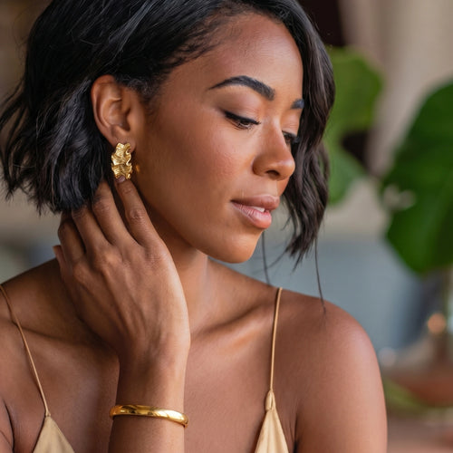 Slim, smooth bangle worn on a wrist, reflecting light elegantly, set against a natural backdrop of green plants.