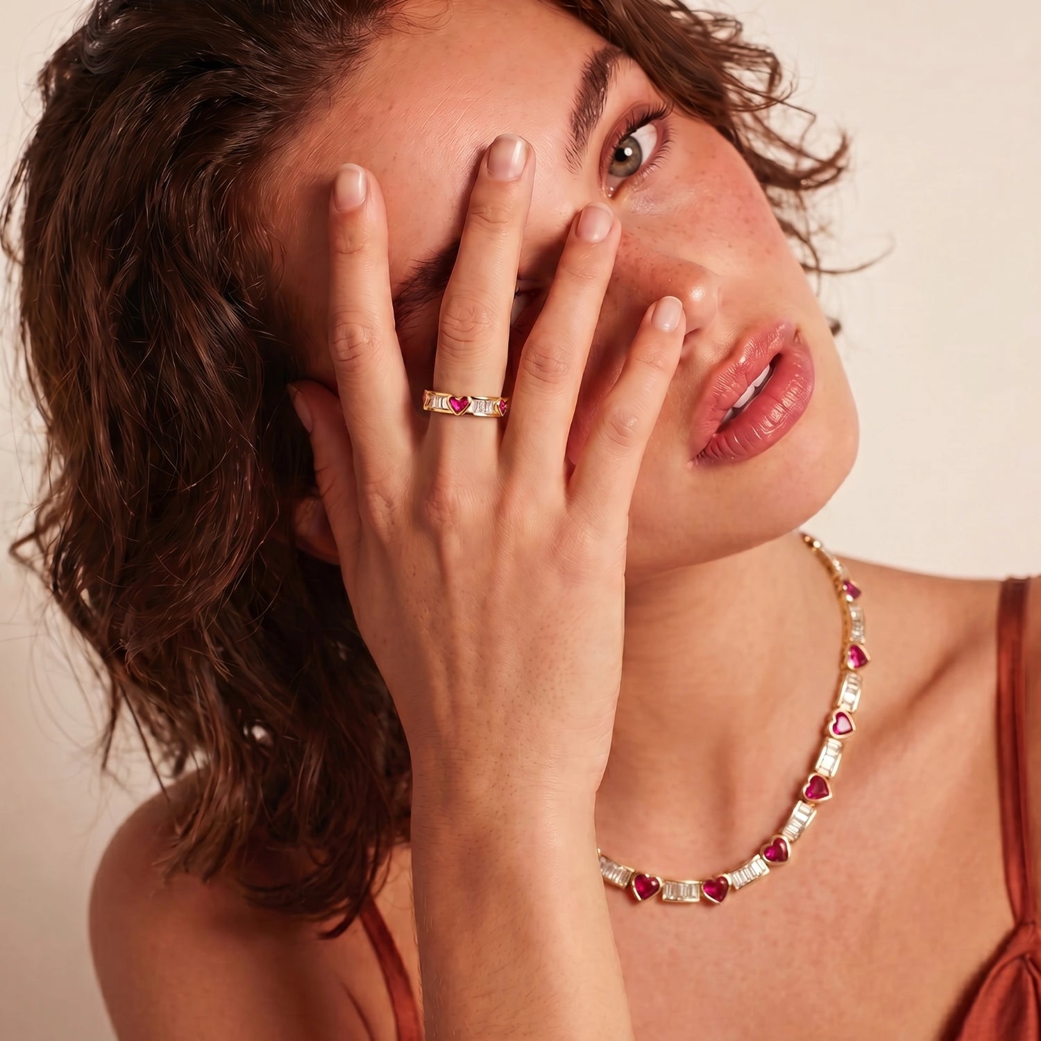 Gold-plated adjustable ring featuring pink heart shapes and clear baguette stones, elegantly showcased on a model's finger.