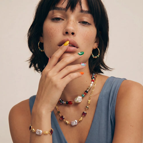 Bracelet showcasing deep red stones, pink freshwater pearls, and hammered gold nuggets, elegantly worn on a wrist.
