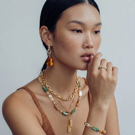 Model showcasing the Sunset Shell Bracelet alongside elegant gold-toned jewellery, featuring hues of amber, green, and cream.