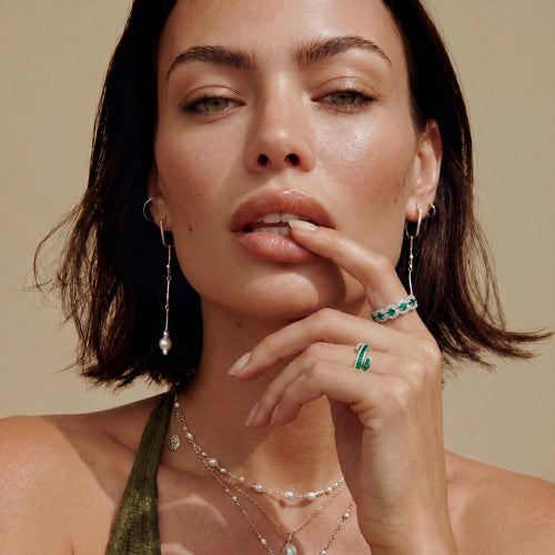 Platinum-plated ring featuring a wave design adorned with deep green zirconia and clear stones, elegantly worn on a finger.