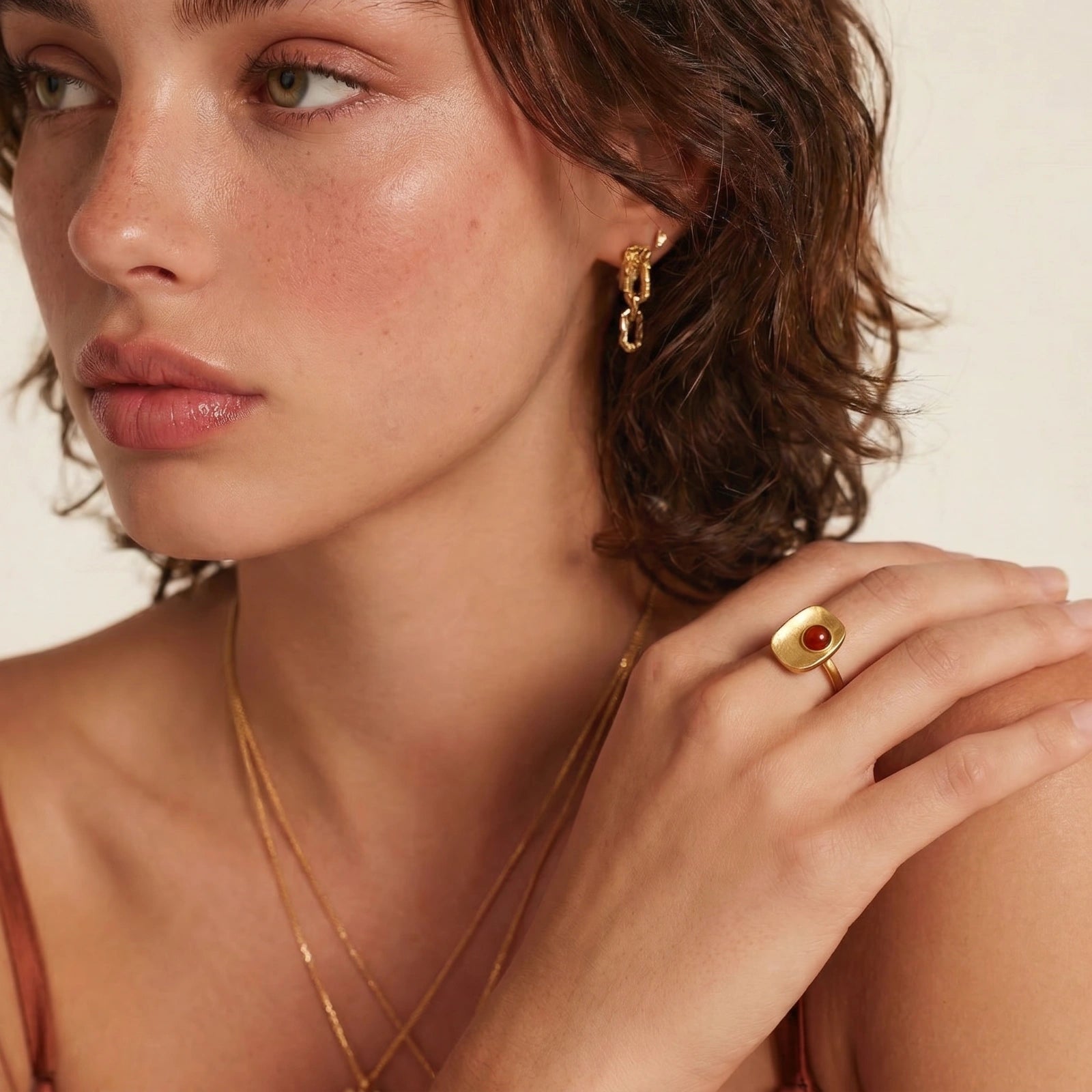 Model showcasing a square ring with a central deep red stone and a gold-coloured band, styled elegantly with layered jewellery.