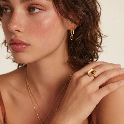 Model showcasing a square ring with a central deep red stone and a gold-coloured band, styled elegantly with layered jewellery.