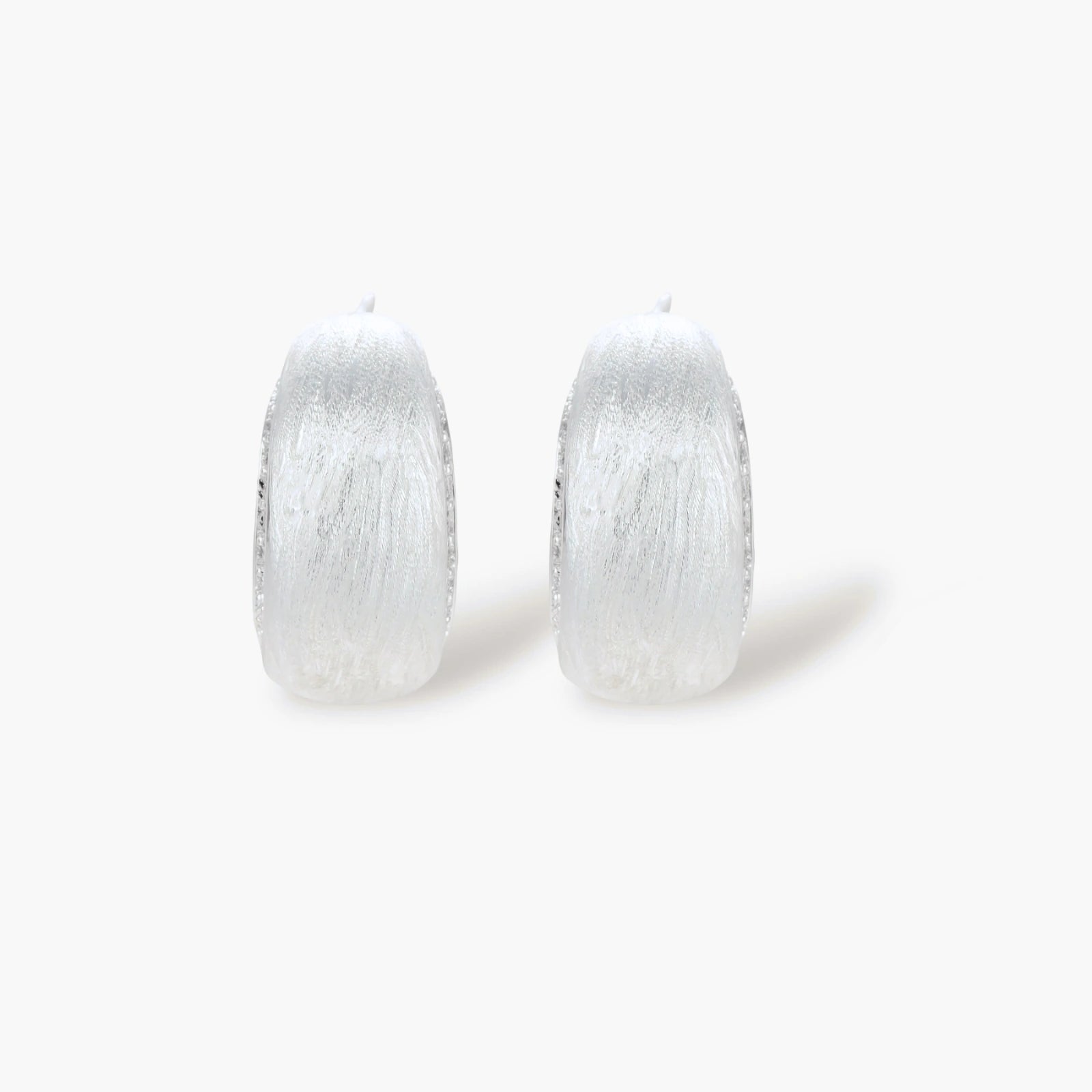 Close-up of small silver-plated hoop earrings with brushed texture and a row of sparkling zircon crystals on white background