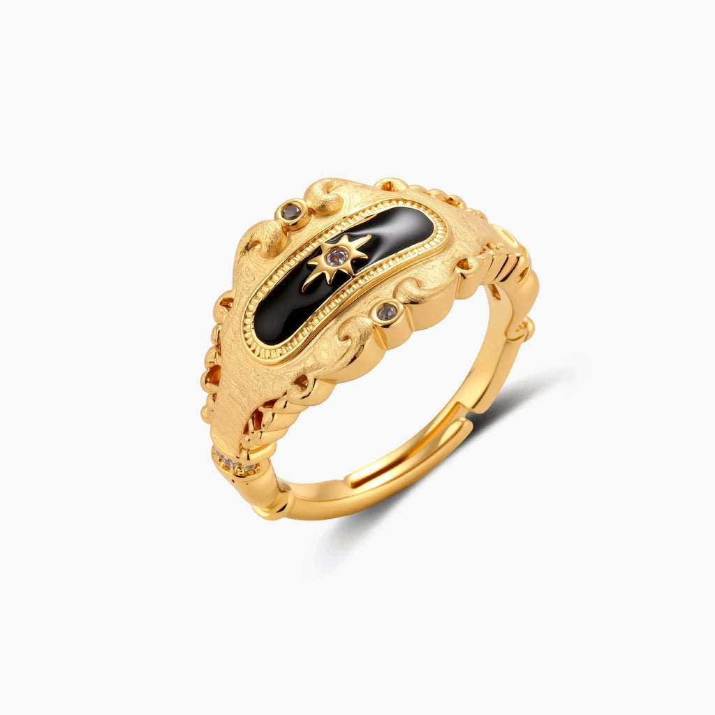 Ornate 18K gold-plated ring with black enamel center featuring star motif and decorative baroque-style edges on white background.
