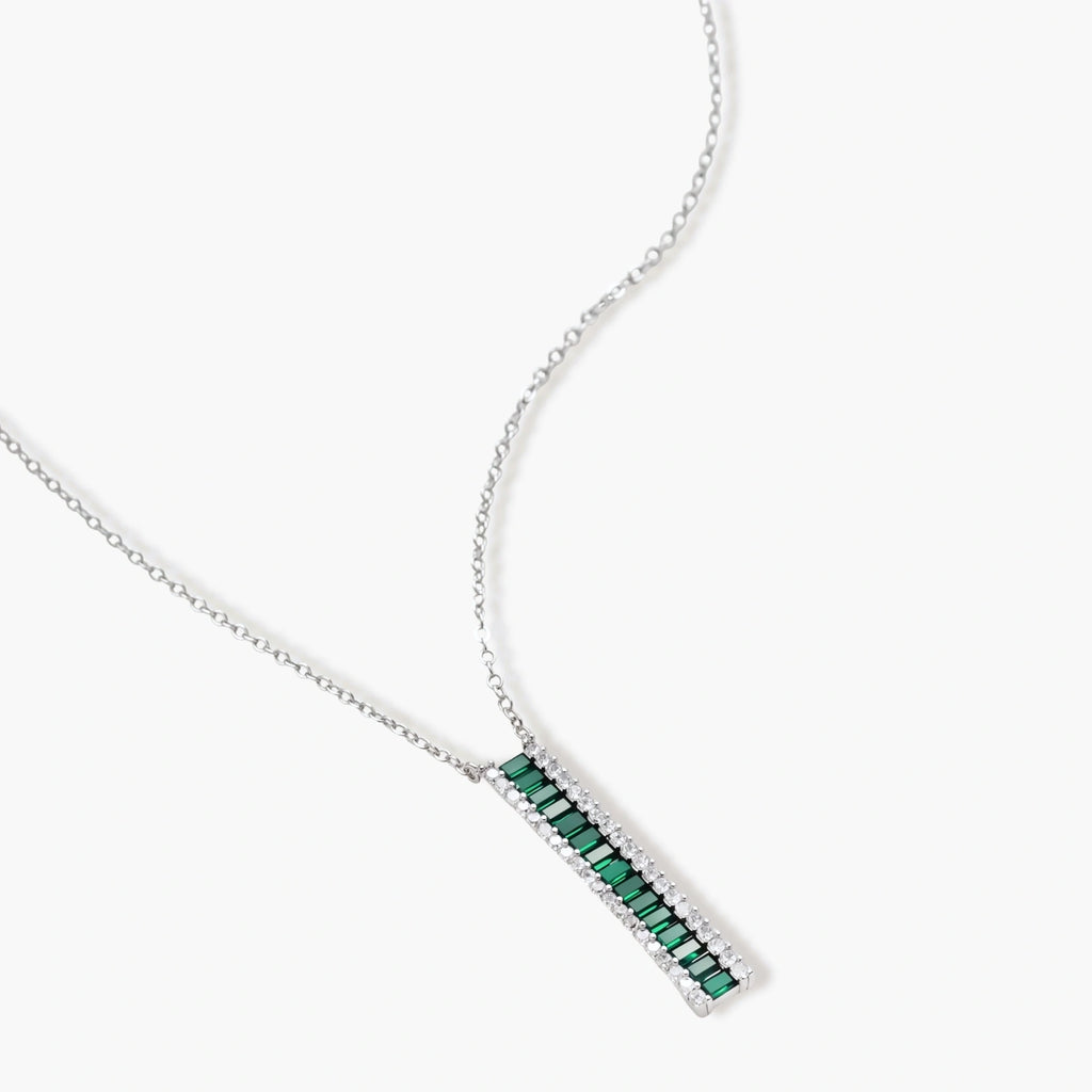 White gold plated jewelry set with emerald green rectangular stones and clear crystals in geometric rows on white background.