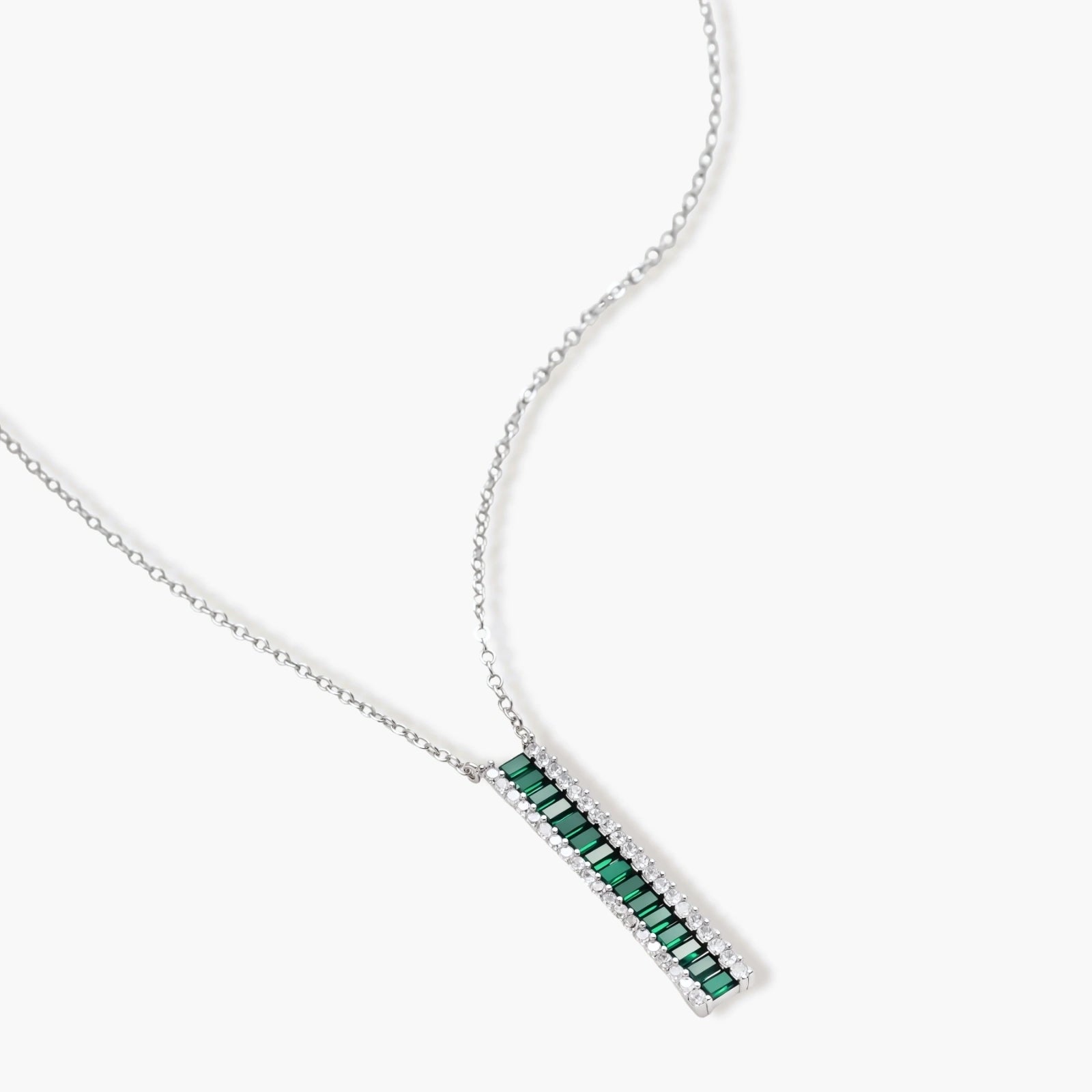 White gold plated jewelry set with emerald green rectangular stones and clear crystals in geometric rows on white background.