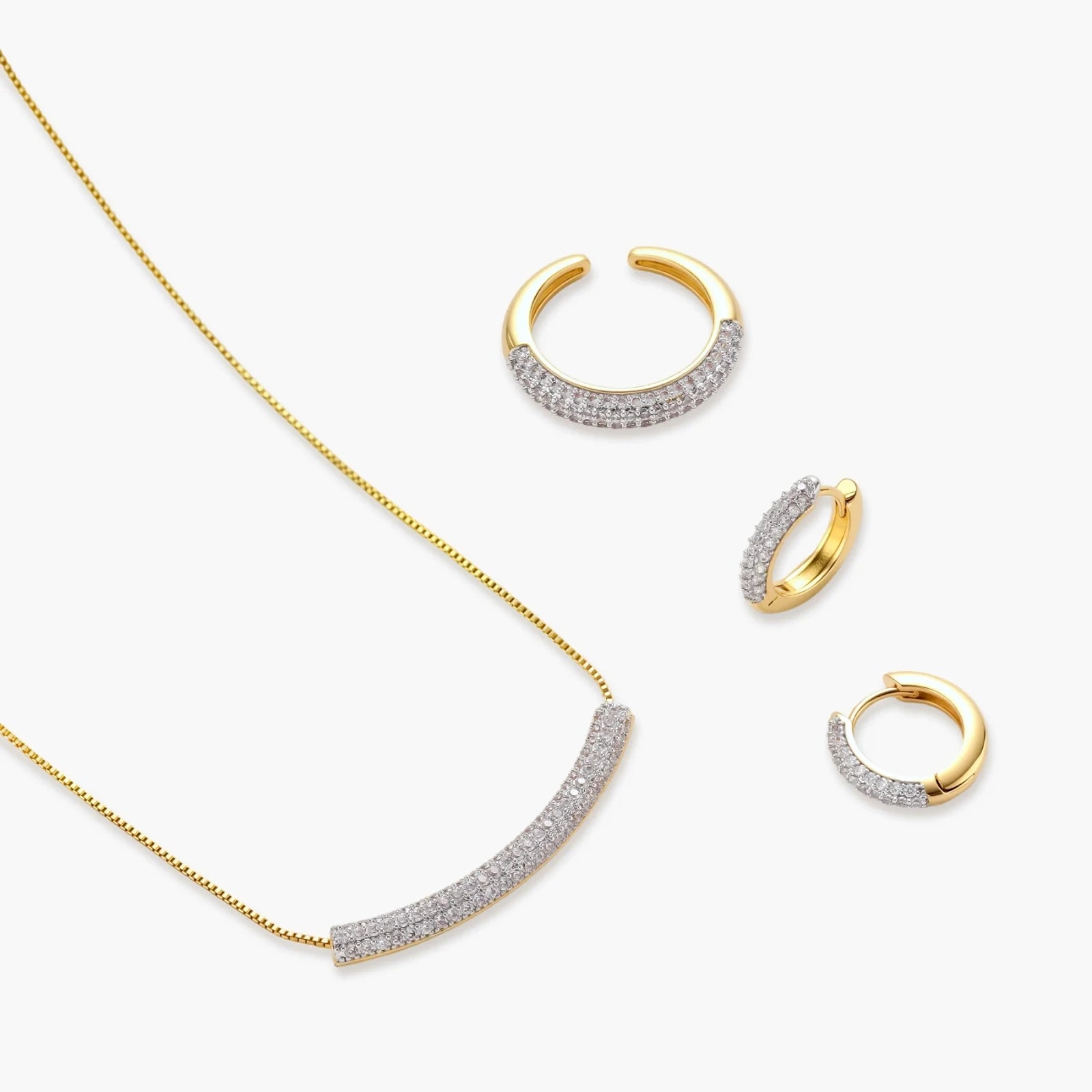 Gold-plated curved necklace, hoop earrings, and adjustable ring with pavé cubic zirconia stones on cream background.