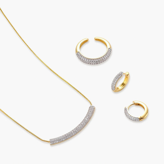 Gold-plated curved necklace, hoop earrings, and adjustable ring with pavé cubic zirconia stones on cream background.