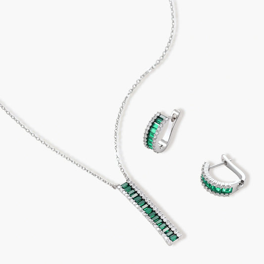 White gold plated jewelry set with emerald green rectangular stones and clear crystals in geometric rows on white background.