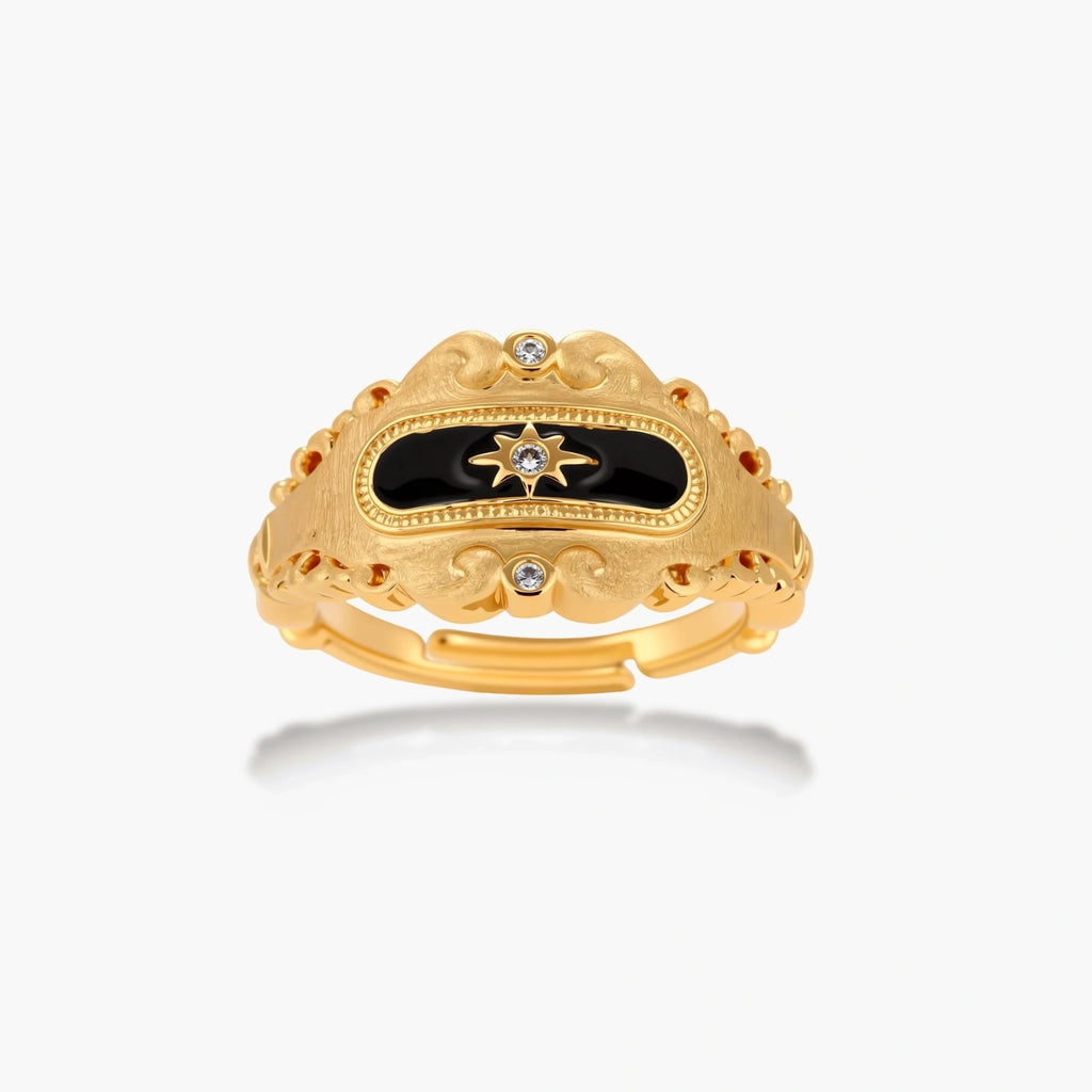 Ornate 18K gold-plated ring with black enamel center featuring star motif and decorative baroque-style edges on white background.