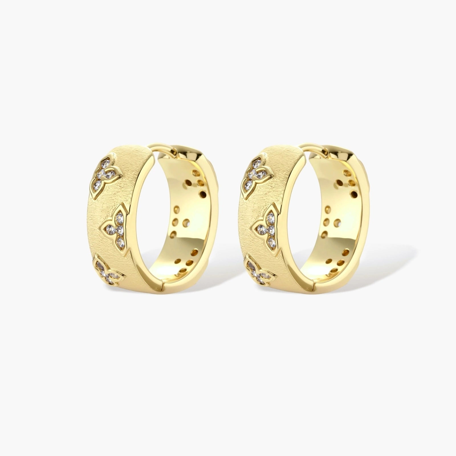 Gold-plated hoop earrings with textured surface and raised floral motifs set with clear zirconia stones on cream background.