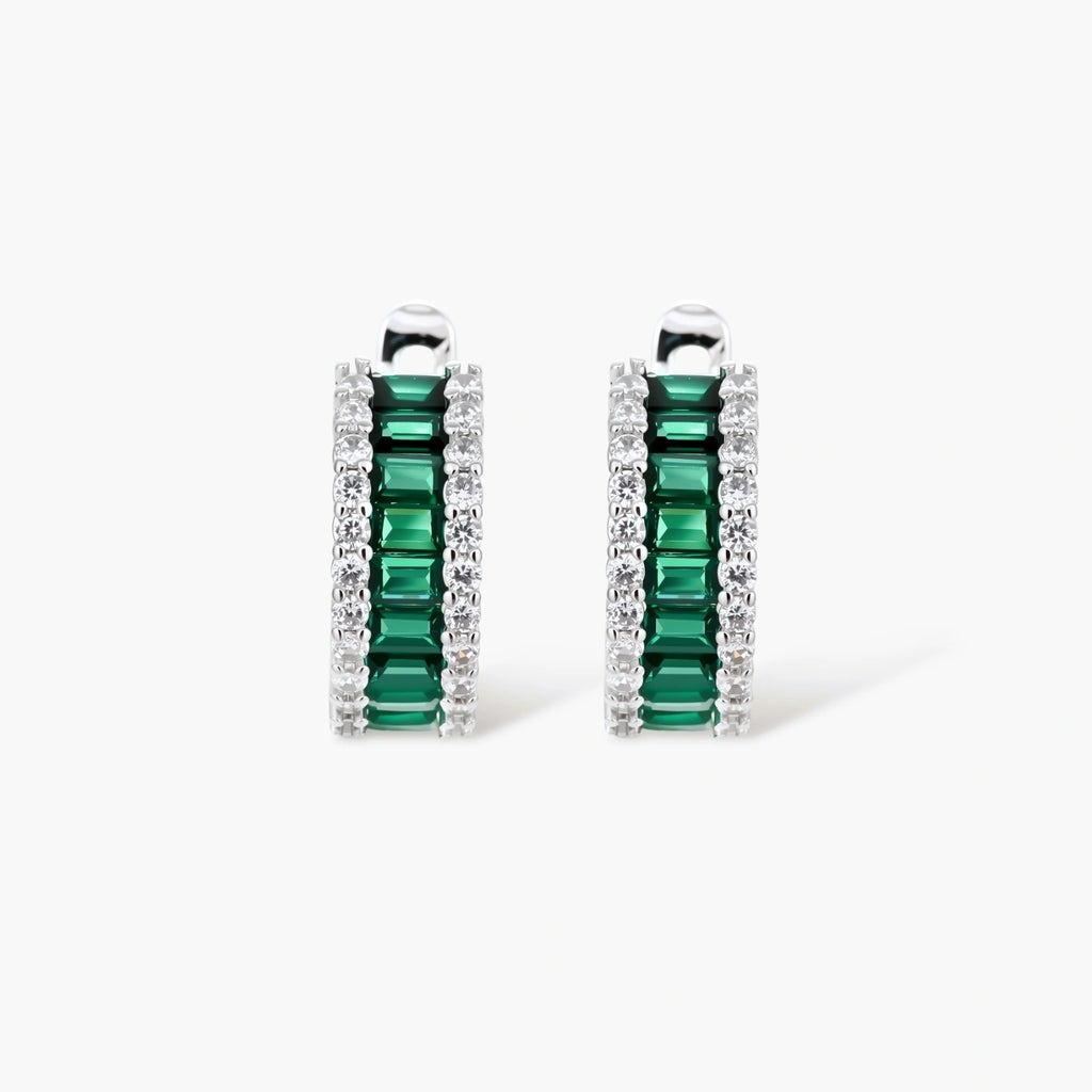 White gold plated jewelry set with emerald green rectangular stones and clear crystals in geometric rows on white background.