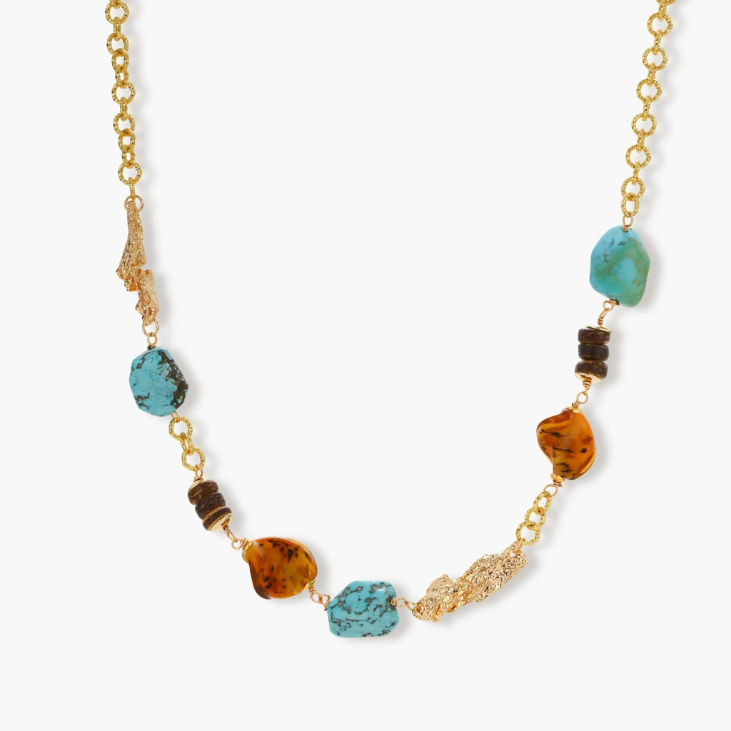 Statement necklace with gold chain, turquoise stones, amber beads, and wooden elements on cream background.
