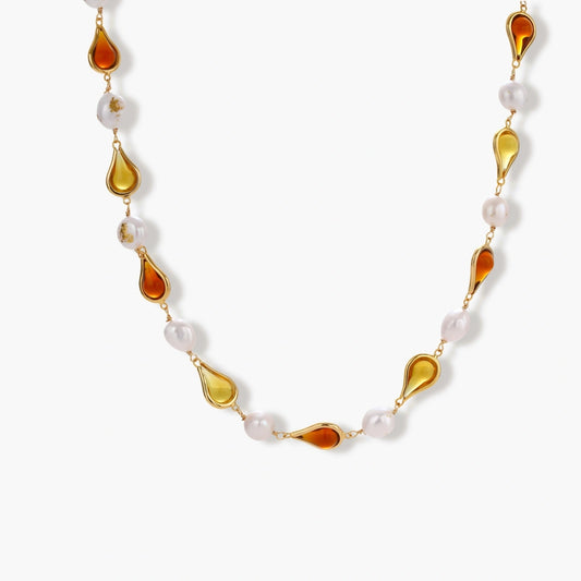 Gold-plated copper necklace with amber teardrop settings and white baroque freshwater pearls on cream background.
