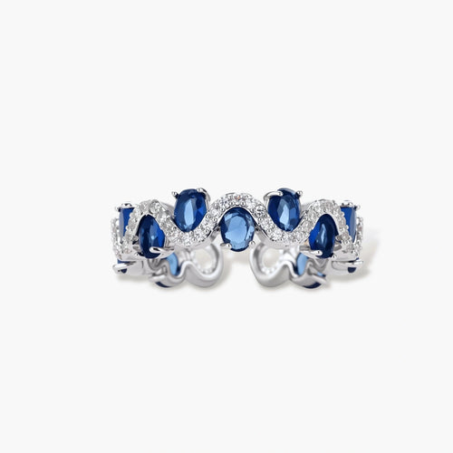 Adjustable ring with blue cubic zirconia stones in flowing wave pattern, copper with platinum plating on white background.