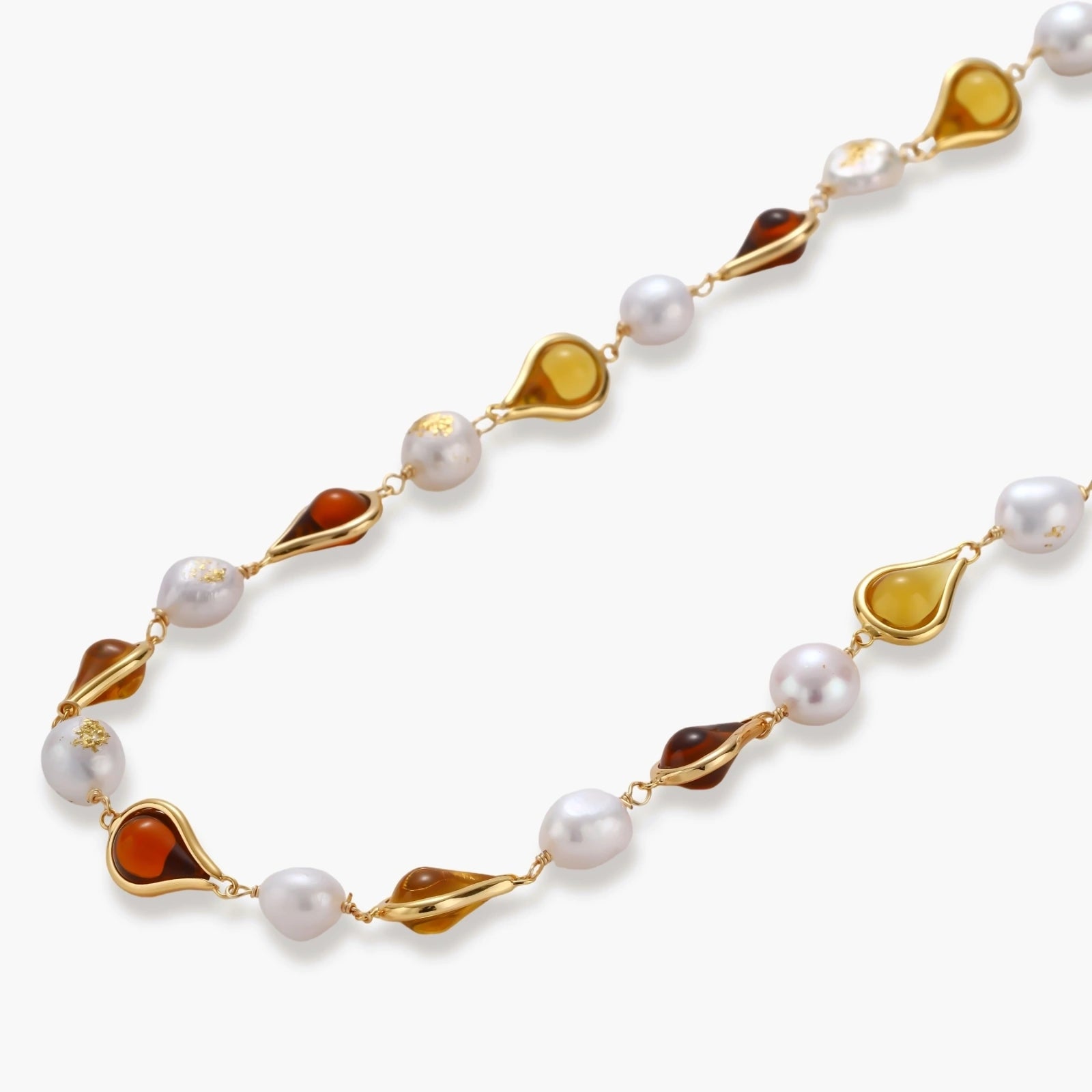 Gold-plated copper necklace with amber teardrop settings and white baroque freshwater pearls on cream background.