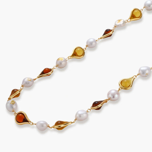 Gold-plated copper necklace with amber teardrop settings and white baroque freshwater pearls on cream background.