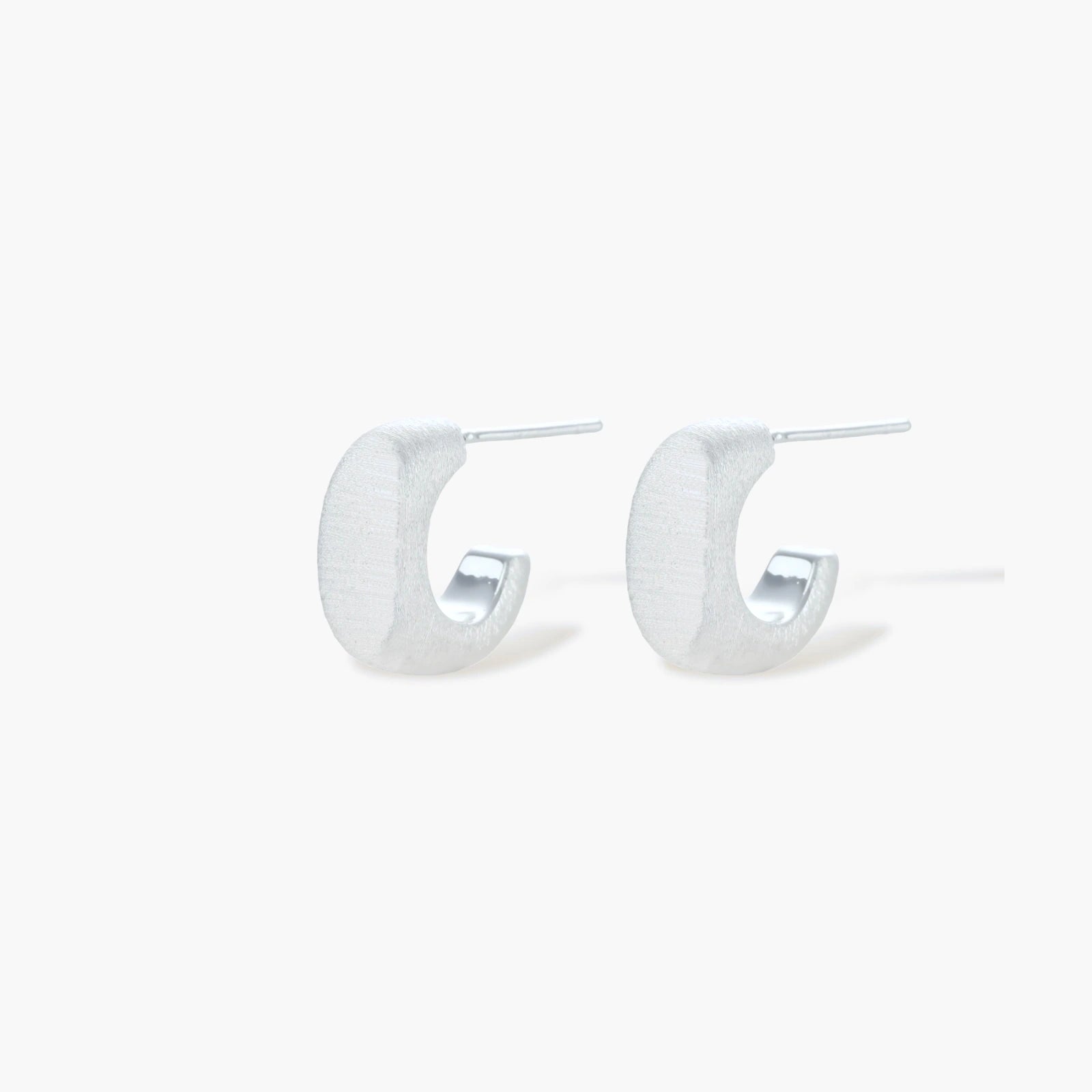 Pair of small silver-plated huggie hoop earrings with clean minimal design on neutral background.