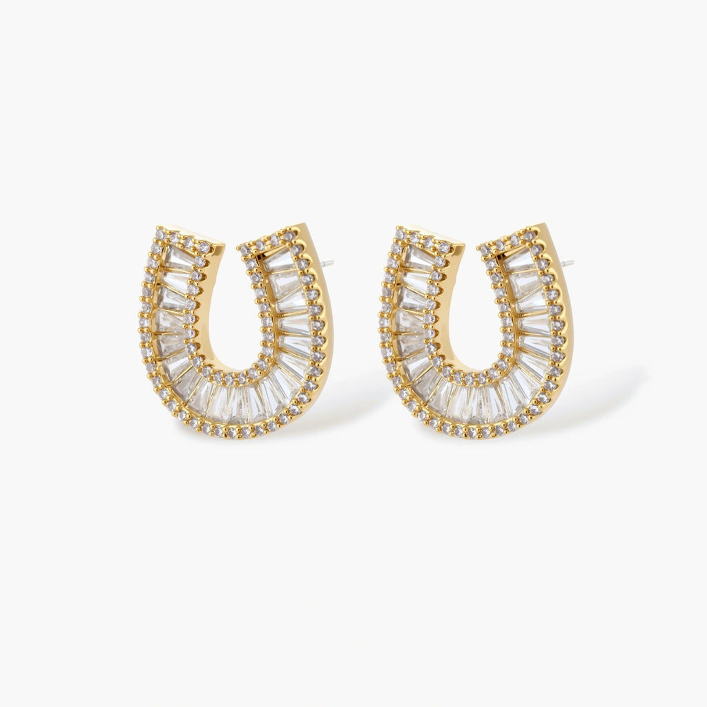 Gold-plated horseshoe necklace and earring set with baguette and round crystals arranged in geometric pattern on white background.
