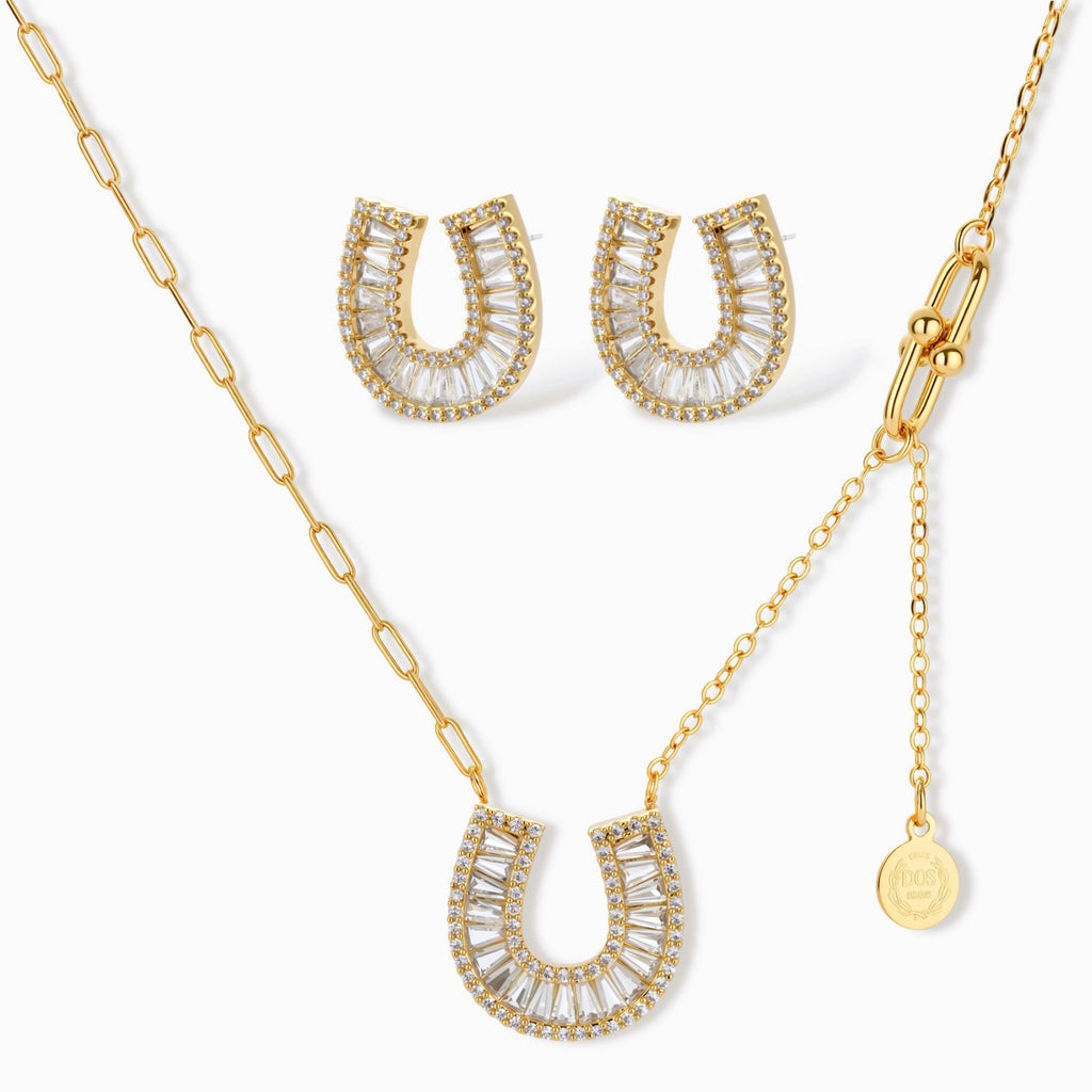 Gold-plated horseshoe necklace and earring set with baguette and round crystals arranged in geometric pattern on white background.