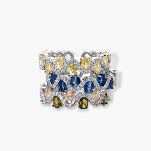 Adjustable ring with blue cubic zirconia stones in flowing wave pattern, copper with platinum plating on white background.