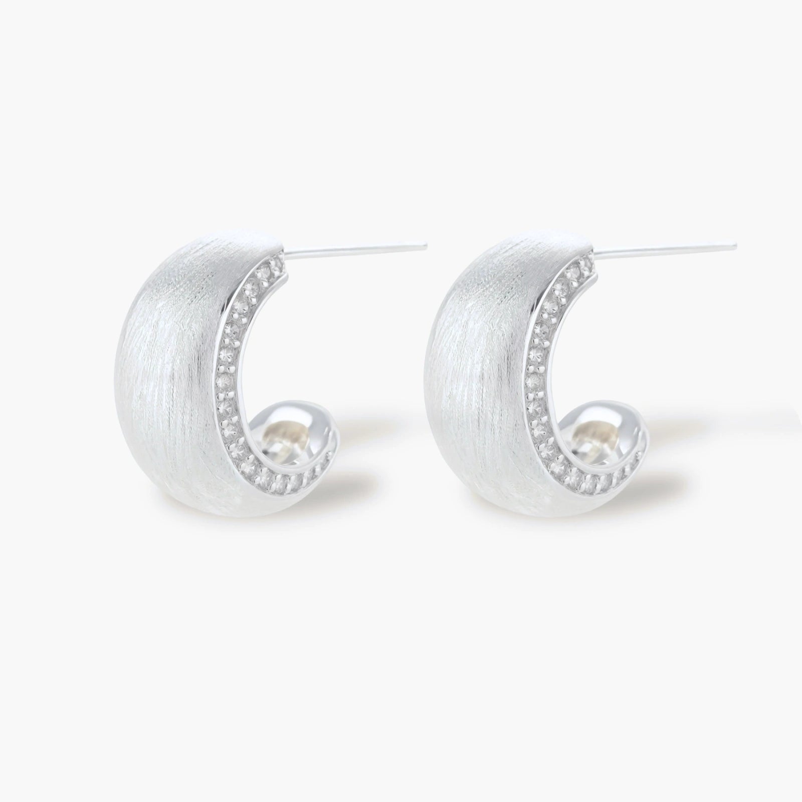 Close-up of small silver-plated hoop earrings with brushed texture and a row of sparkling zircon crystals on white background