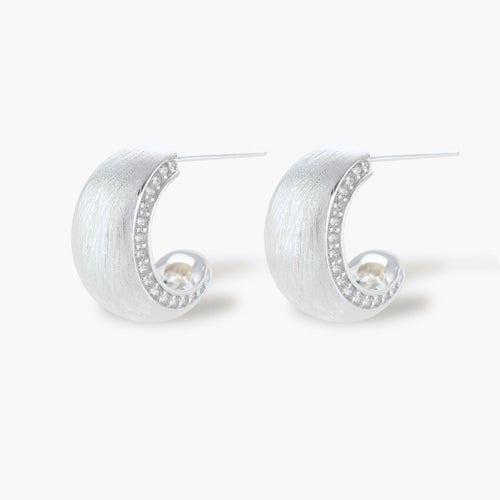 Close-up of small silver-plated hoop earrings with brushed texture and a row of sparkling zircon crystals on white background