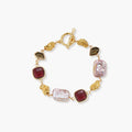 18k gold-plated copper bracelet with burgundy stones, smoky quartz, baroque pearls and ornate golden charms on white background.