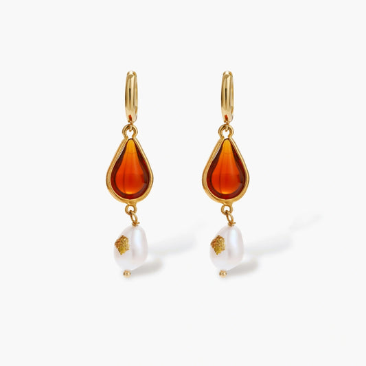 Gold-plated drop earrings featuring amber teardrops and white baroque pearls on light background.